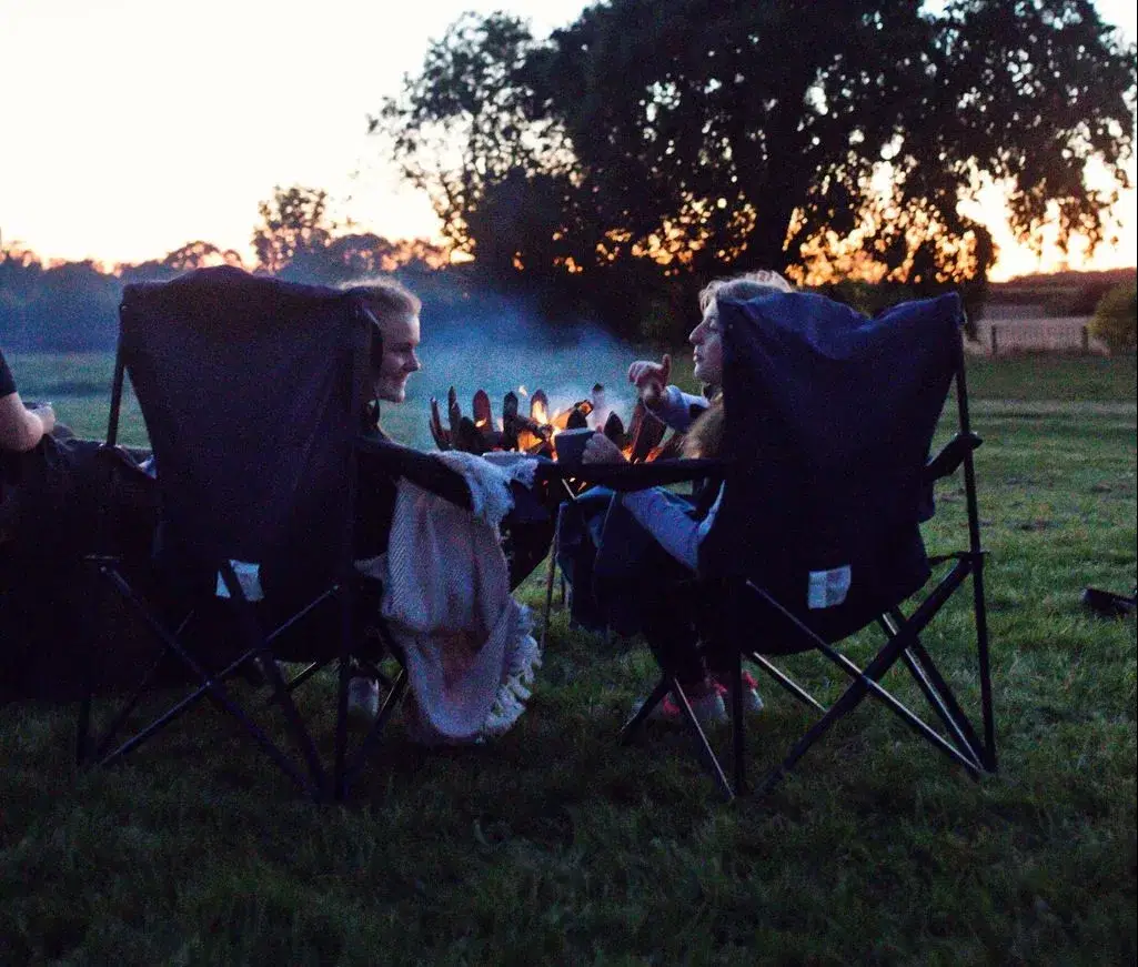 two girls chatting round a fire pit watching the sun set