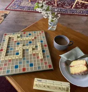 Scrabble board game spelling out the word Glamping with a cup of tea and a slice of cake